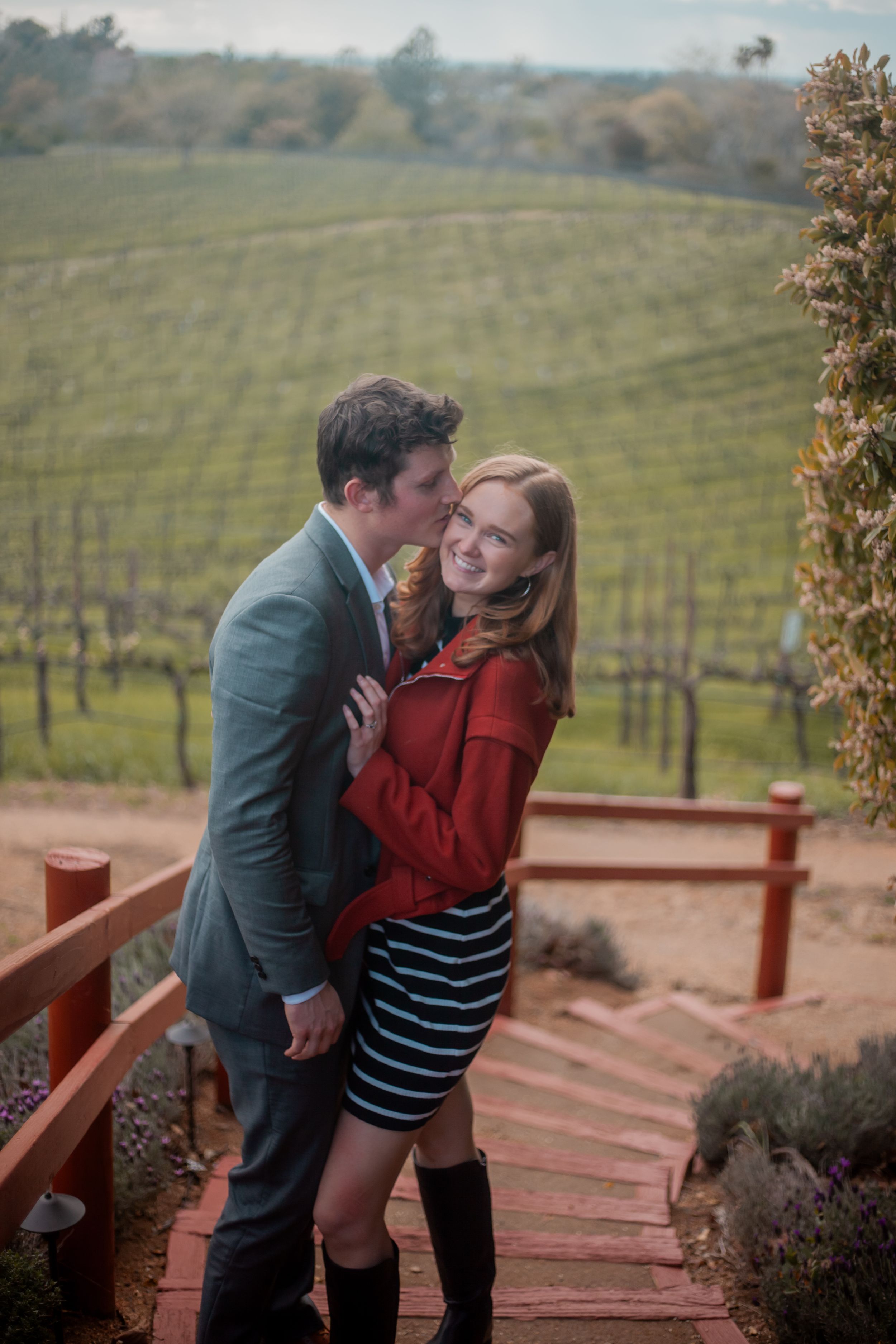 Romantic couple sharing tender moment on stairs overlooking vineyard.
