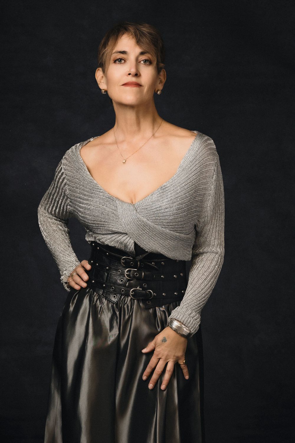 Studio portrait against dark backdrop showing wrap sweater paired with dramatic high-waisted satin skirt and corset belt.