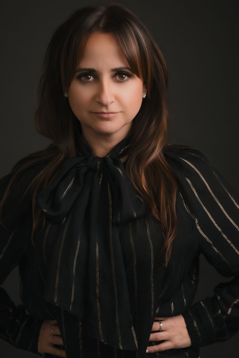 Professional studio portrait of someone in a black bow-tied top with metallic pinstripes against dark background.