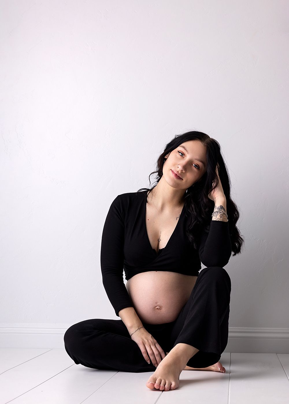 A pregnant woman in black clothing poses artistically against a white wall in a series of four connected photos.