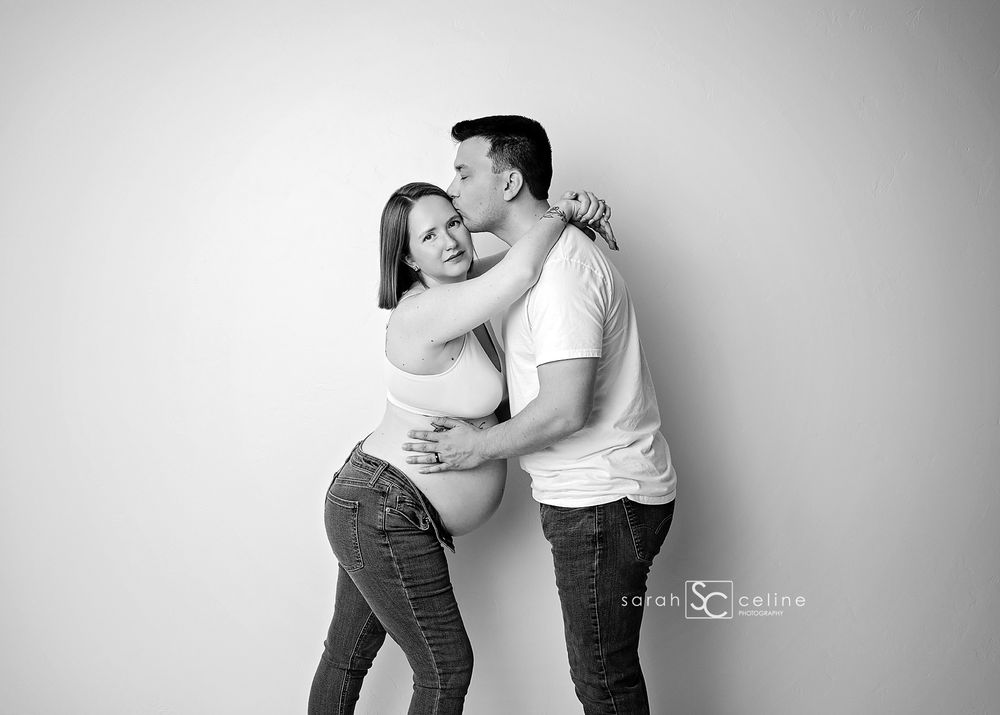 Black and white maternity photo of a couple embracing, man kissing woman's head while she holds her baby bump.