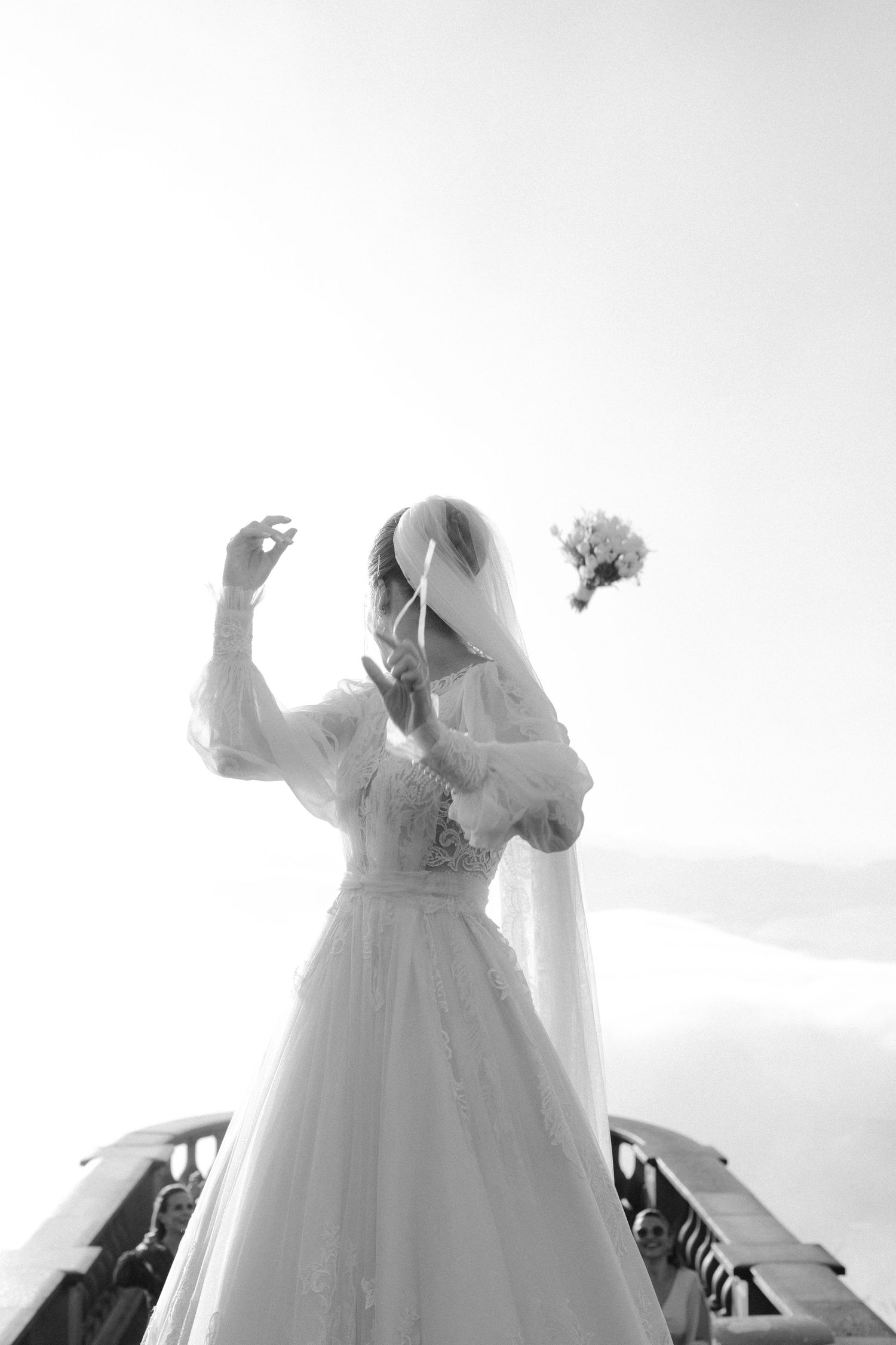 A ethereal black and white photo of a bride in a flowing white dress tossing her bouquet.