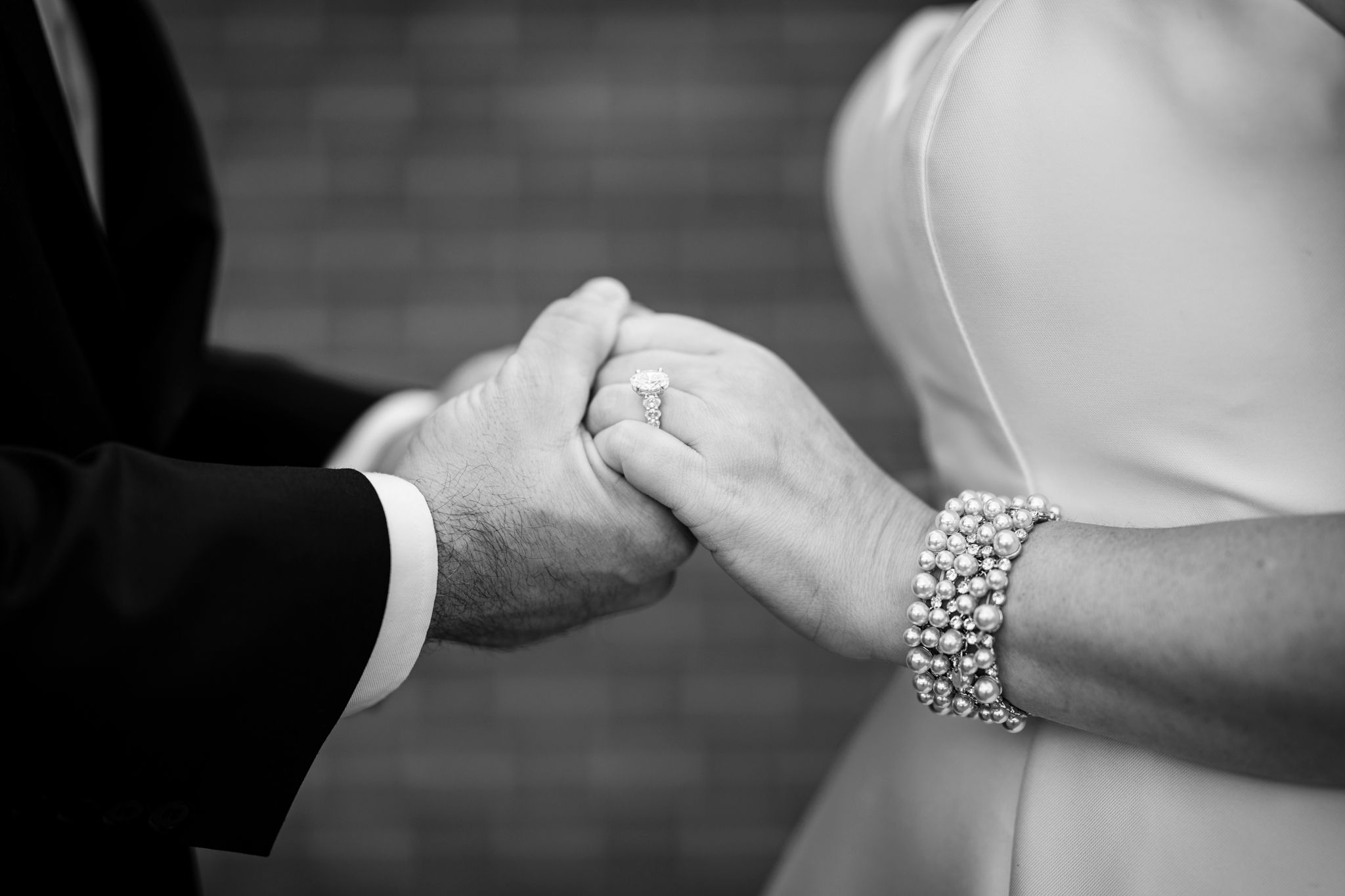 Close up black and white shot of hands clasped together with a bracelet and formal attire.
