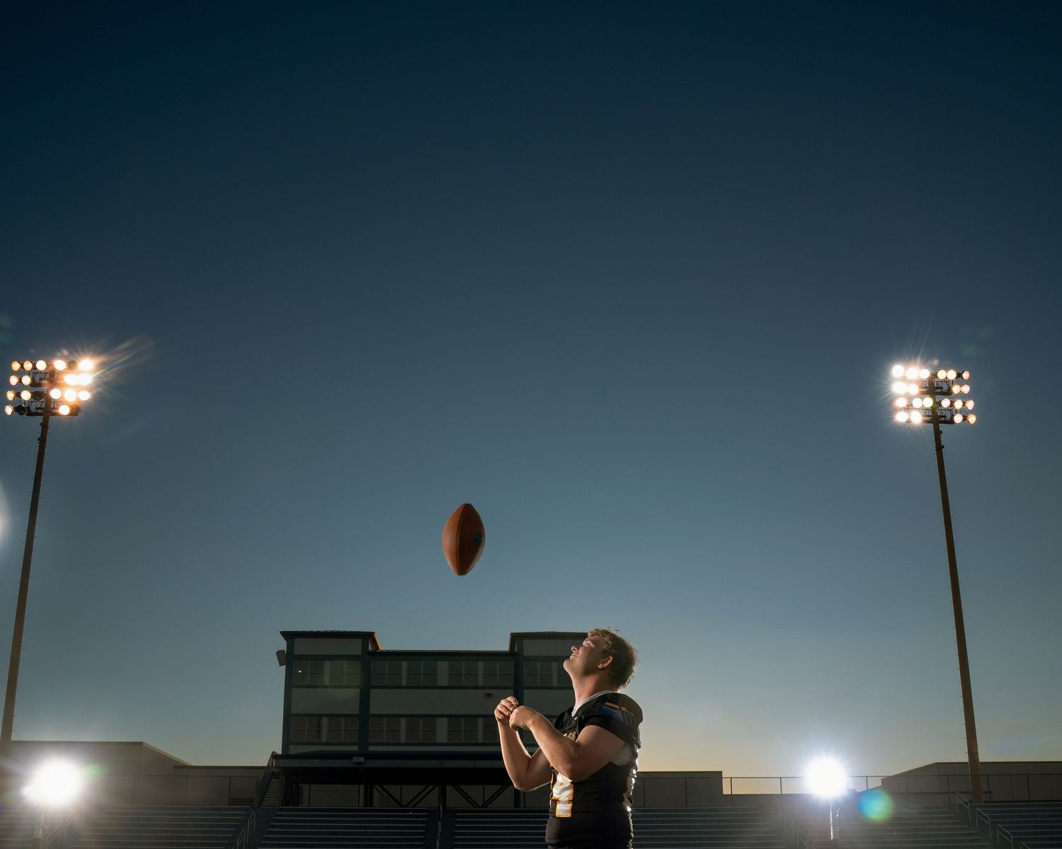 Football field goal attempt silhouetted against dark evening sky with stadium lights glowing.