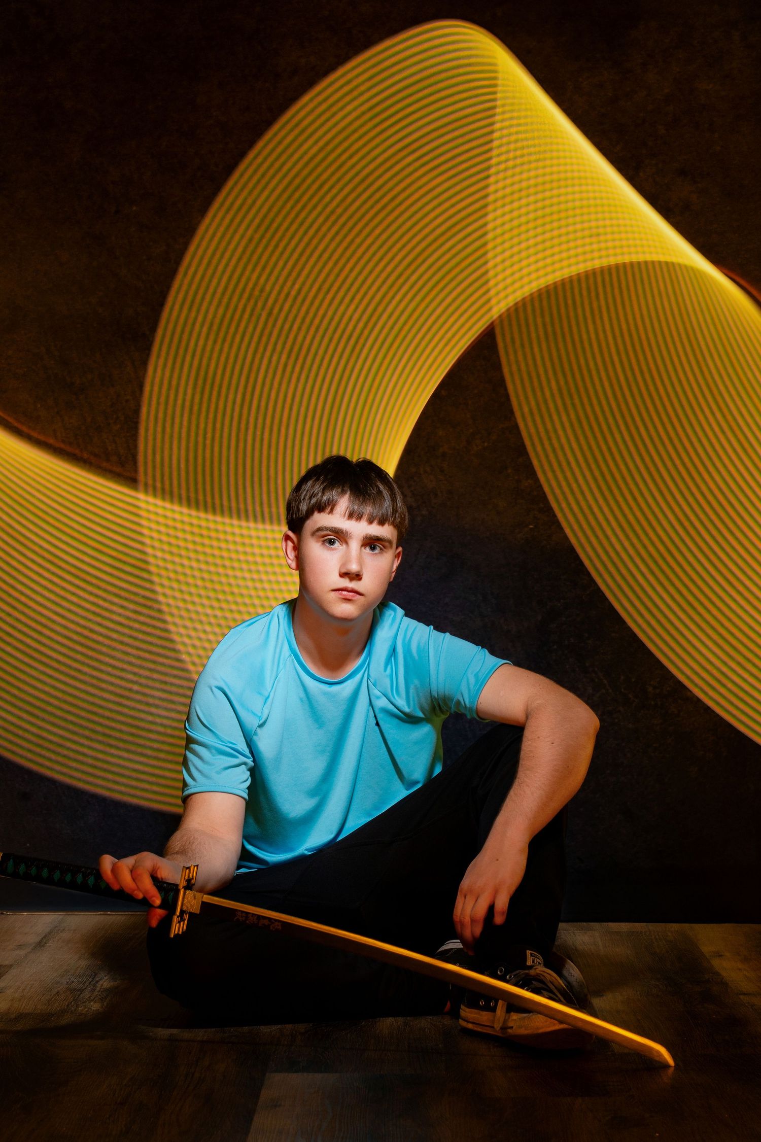 Light painting photography shows a person in turquoise shirt creating glowing yellow light trails against dark background.
