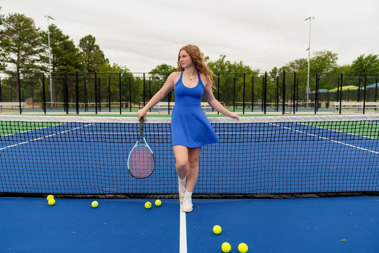 Tennis player in blue outfit practicing serves and drills on outdoor blue court with scattered yellow tennis balls.