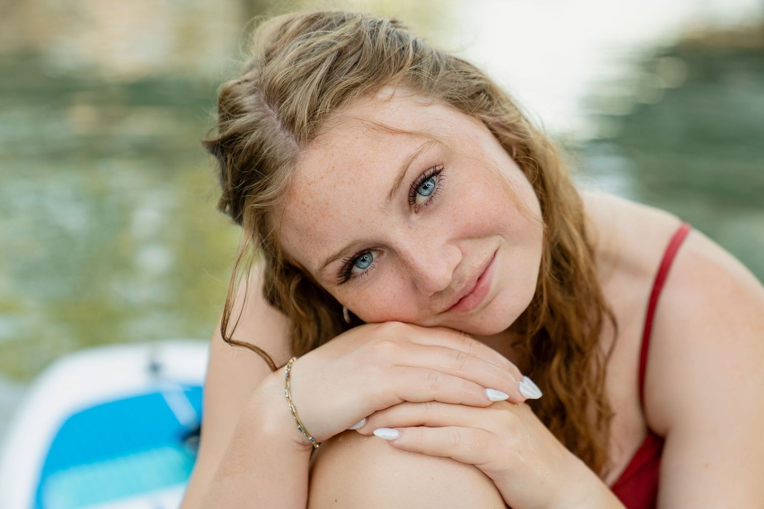 A person in a red top poses playfully with different facial expressions by the water.
