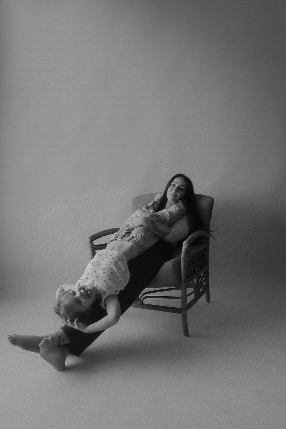 Black and white photo of two women posing together on a rattan chair in a studio setting.