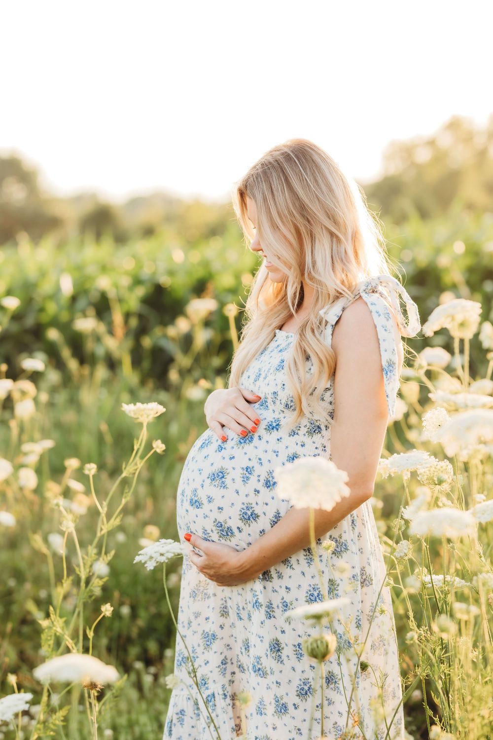 Pregnant woman in floral dress poses in wildflower meadow during sunset New Haven, CT.