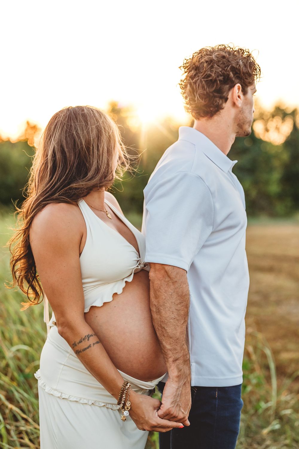 A couple poses together in a golden field at sunset wearing white and blue outfits for romantic photos in New Haven, CT