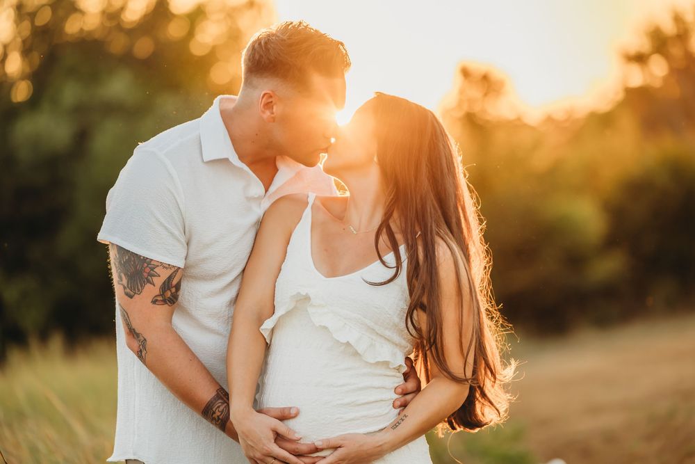 Couple embraces tenderly during golden hour sunset in a grassy field with warm summer lighting close to Hamden, CT