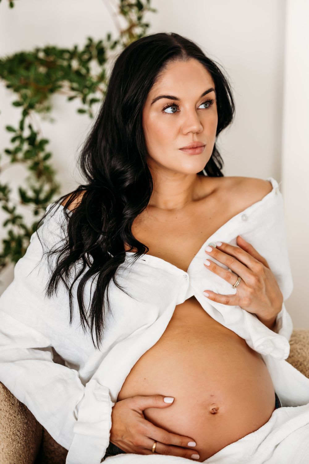Maternity photo of an expectant mother in a white button-down shirt cradling her bare pregnant belly against a light background in New Haven
