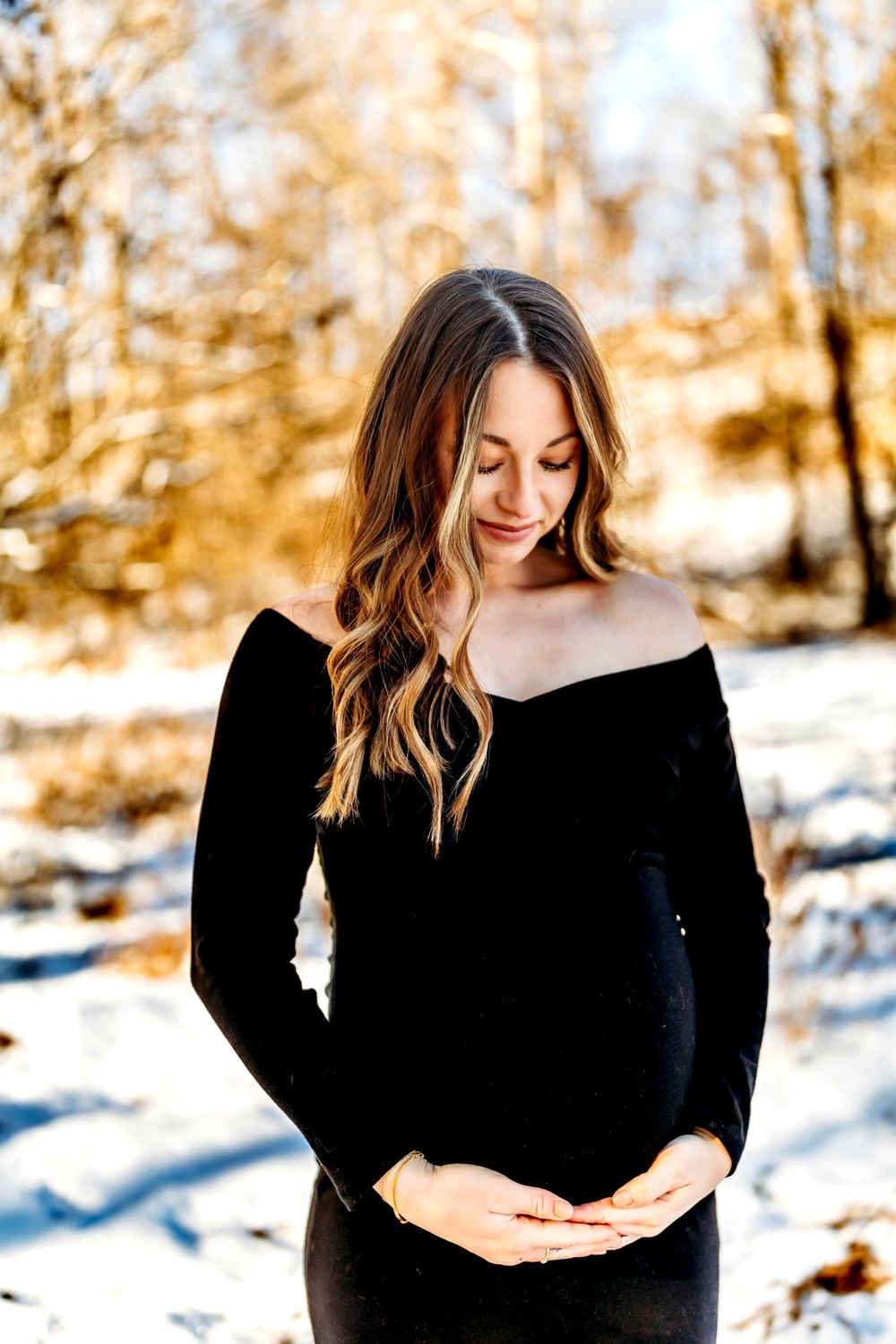 Winter maternity portrait with woman in black off-shoulder sweater against snowy background Hartford, CT.