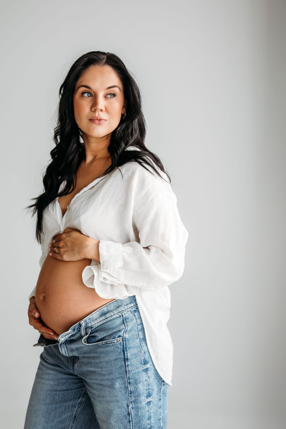 A maternity photoshoot featuring a white button-down shirt and light wash denim jeans against a neutral background close to Branford, CT