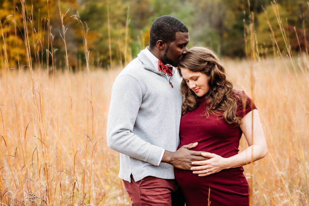 A romantic couple embraces in a golden field during sunset, wearing burgundy and white outfits in New Haven, Connecticut