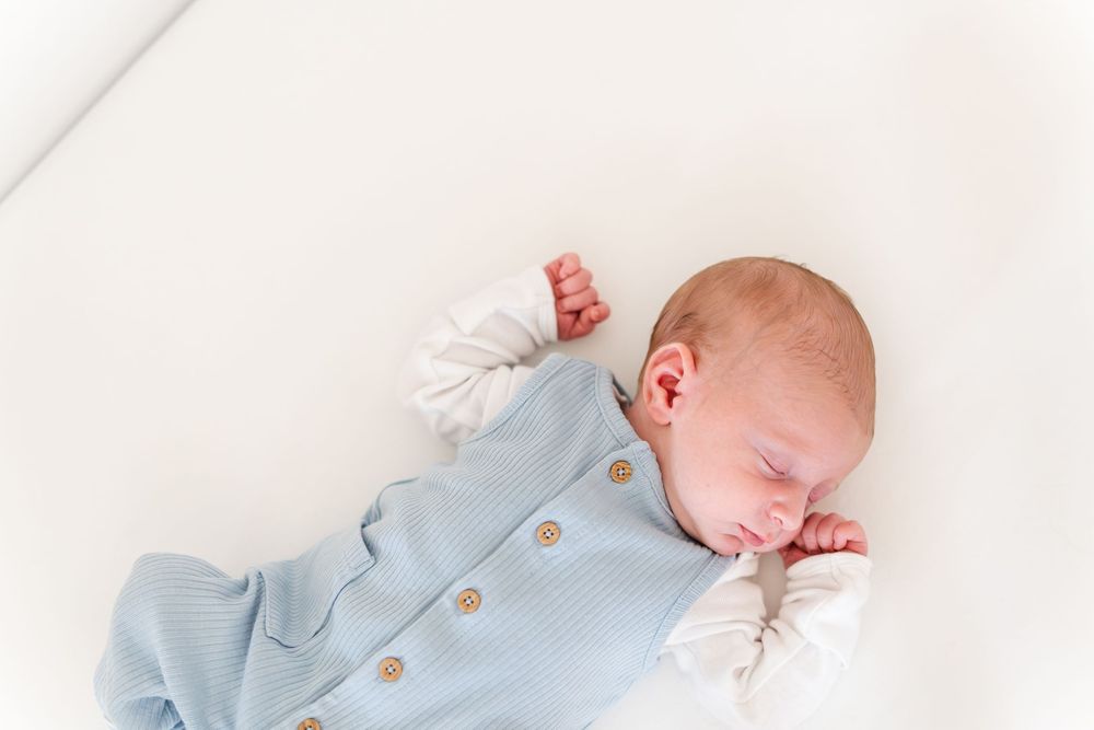 Newborn baby sleeping peacefully in a light blue knit romper on a white background.