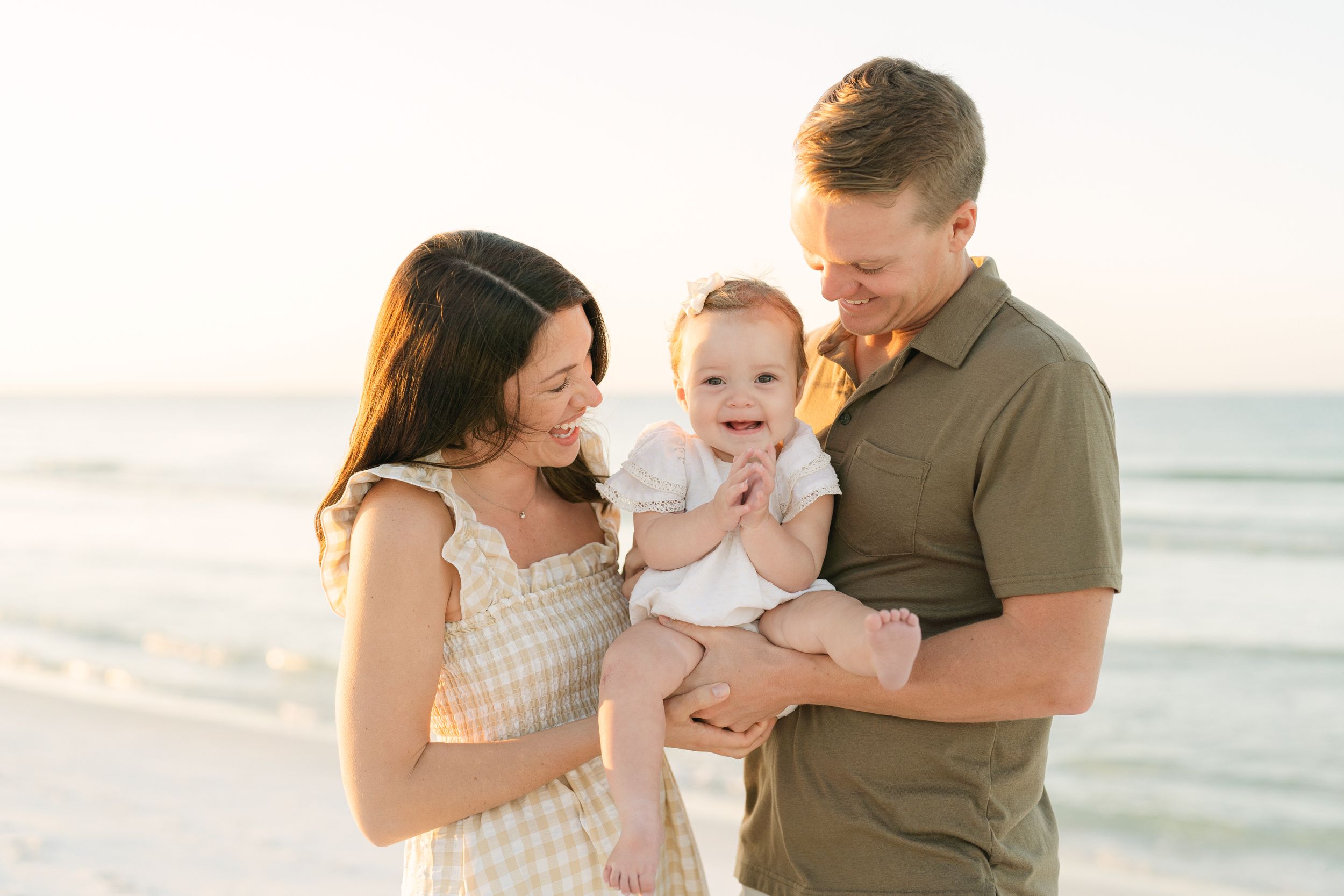Family shares tender moment together on beach at sunset with baby.