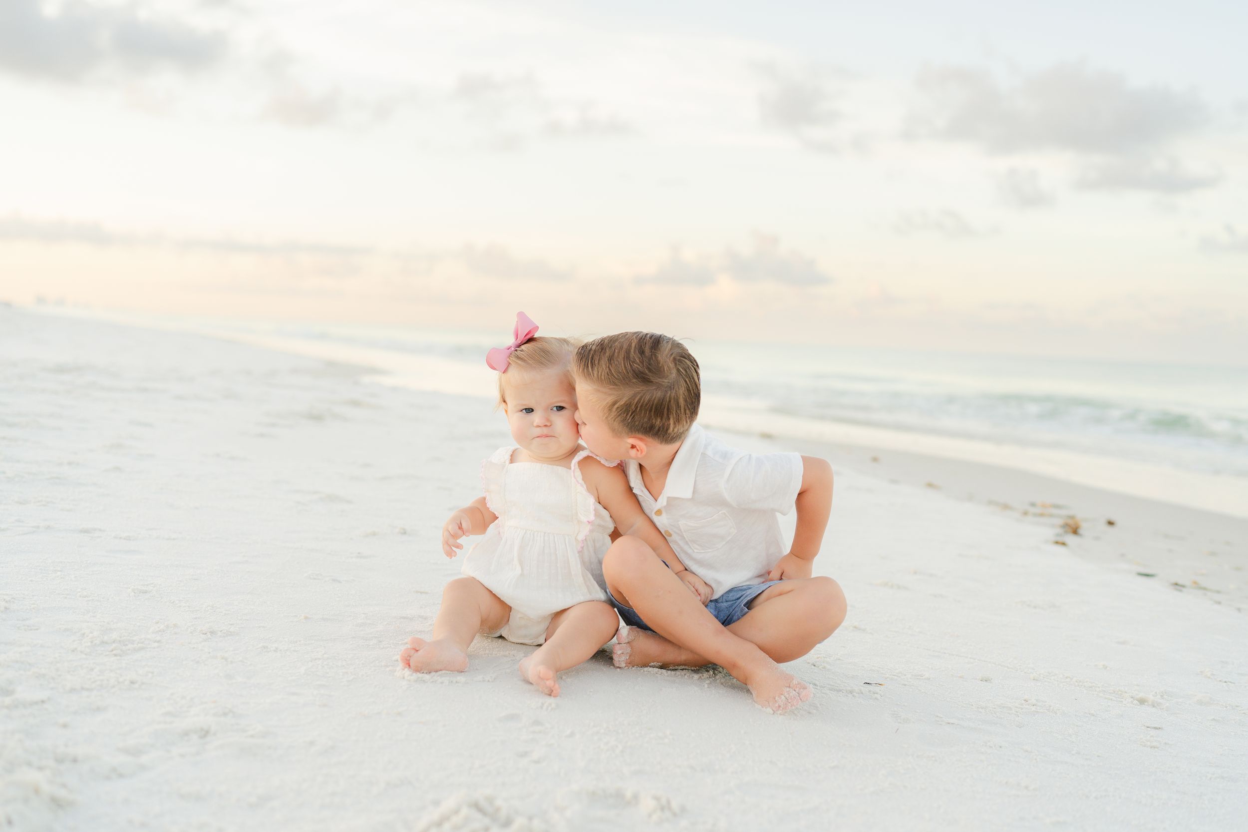 Two children sit together playing in white sand on sunny beach.