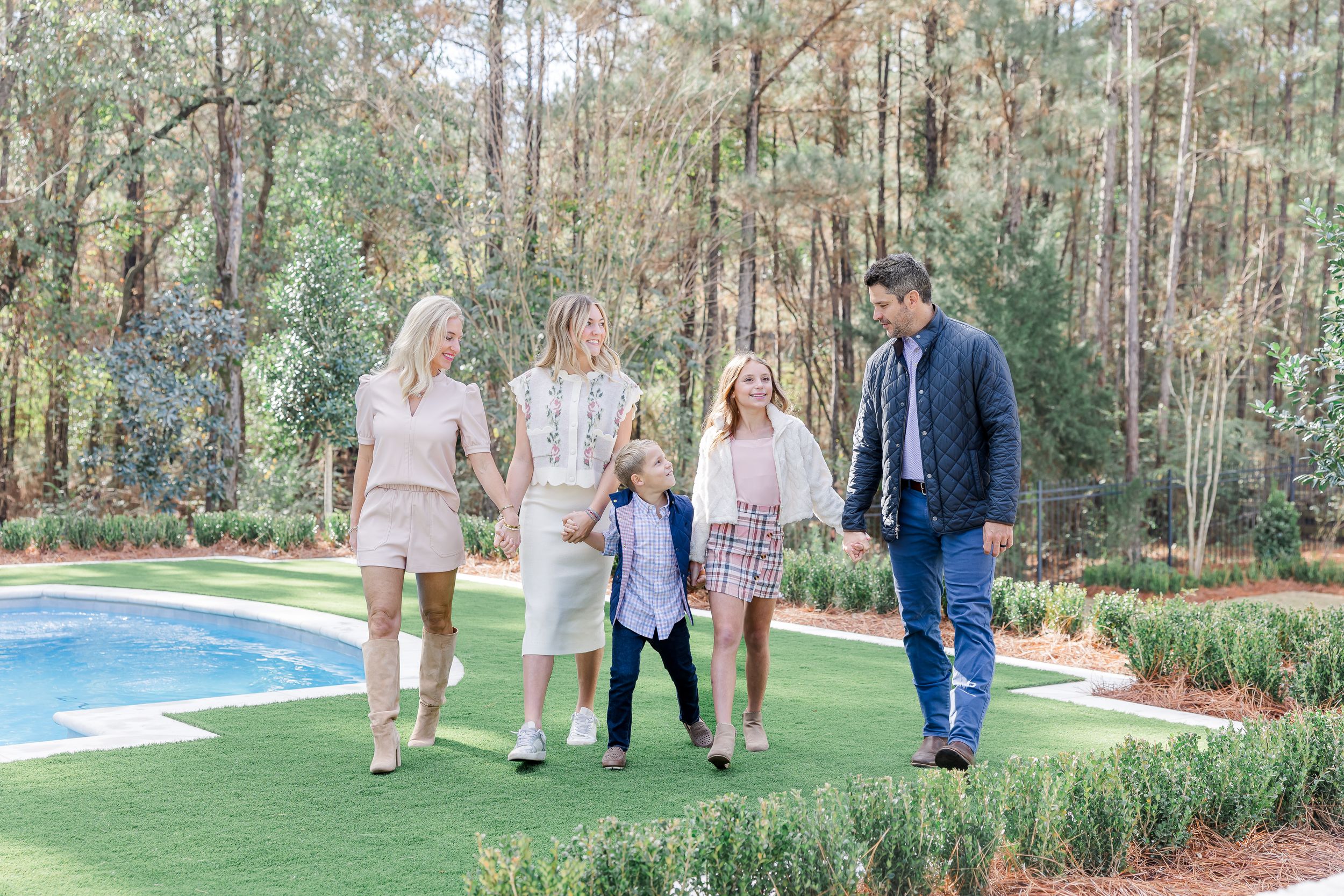 A group walks together on a landscaped lawn beside a swimming pool with pine trees in the background.