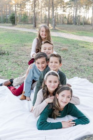 A group of children laying on a white blanket outdoors in a wooded area during golden hour.