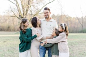 A family shares joyful moments together in a sunny field during an outdoor photo session.