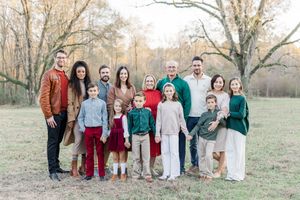 A large family group poses together outdoors in coordinated outfits of red, green and white against a natural autumn backdrop.