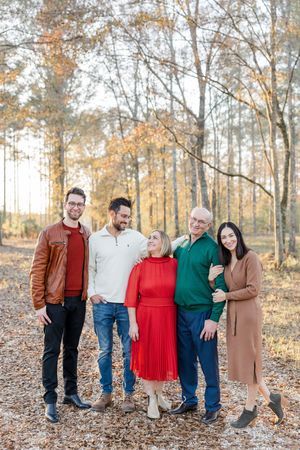 A group poses together outdoors during autumn with fallen leaves and bare trees in the background.