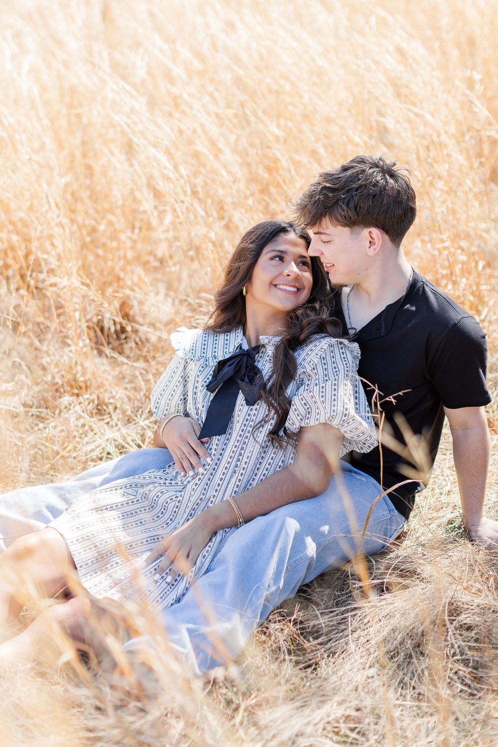 Romantic couple lying together in golden sunlit field of tall grass during outdoor photo session.