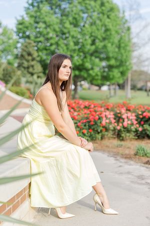 Fashion portraits in yellow dress near blooming rose garden pathway.