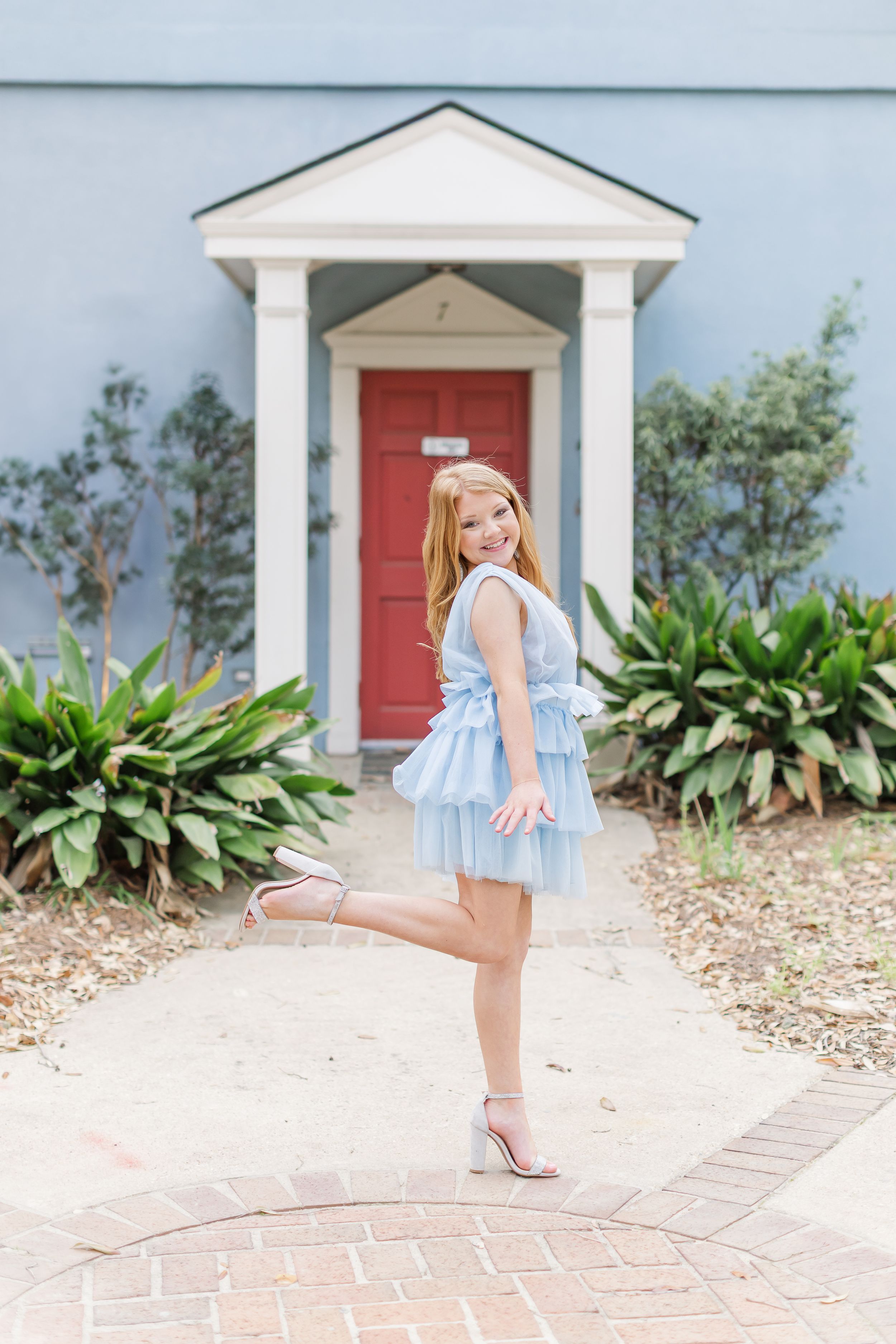 A series of four photos showing a small child in a blue dress twirling and playing on a brick walkway near a white house.