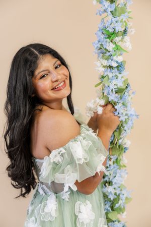 Portrait of someone in a mint green off-shoulder dress with ruffles posing with blue and white floral garland decorations.