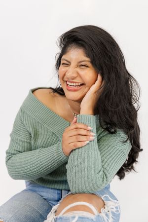 A person wearing a sage green sweater and jeans poses with candid laughter in a series of casual portraits.
