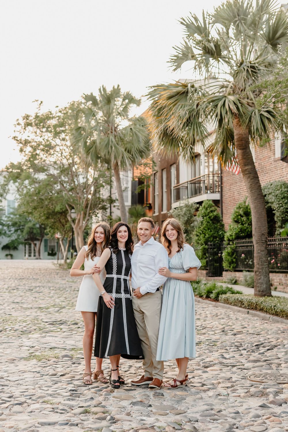 Group of friends walking along a cobblestone path lined with palm trees and historic buildings at sunset.