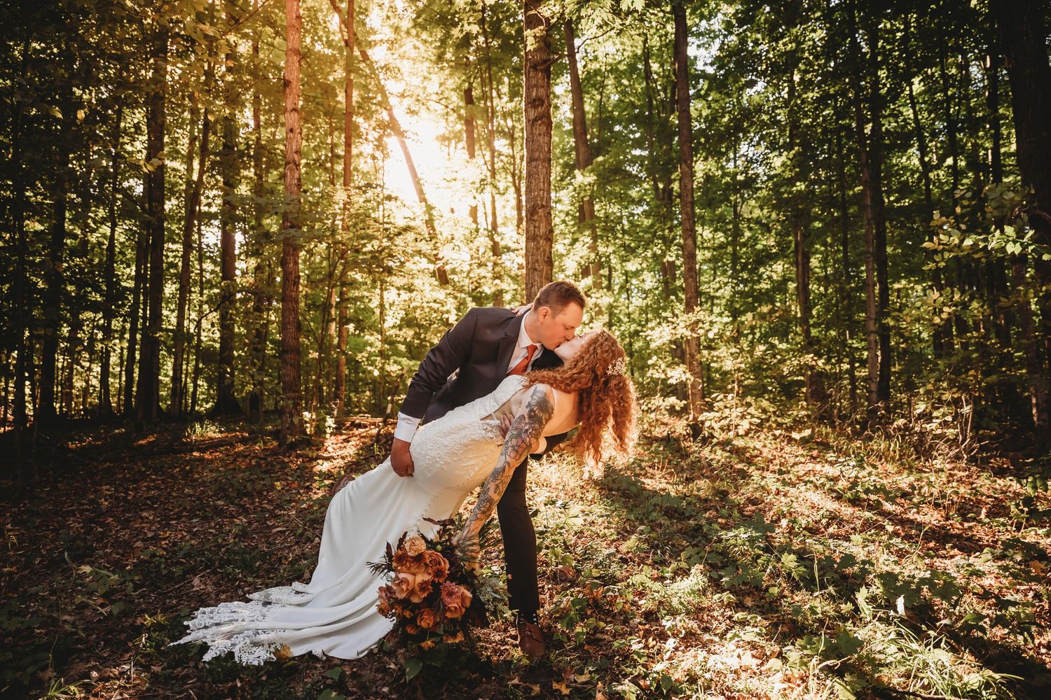 Romantic wedding photography in sunlit forest with golden rays streaming through trees.