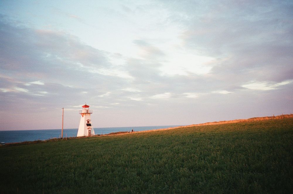 A lighthouse stands on a grassy hill against a moody cloudy sky at dusk.