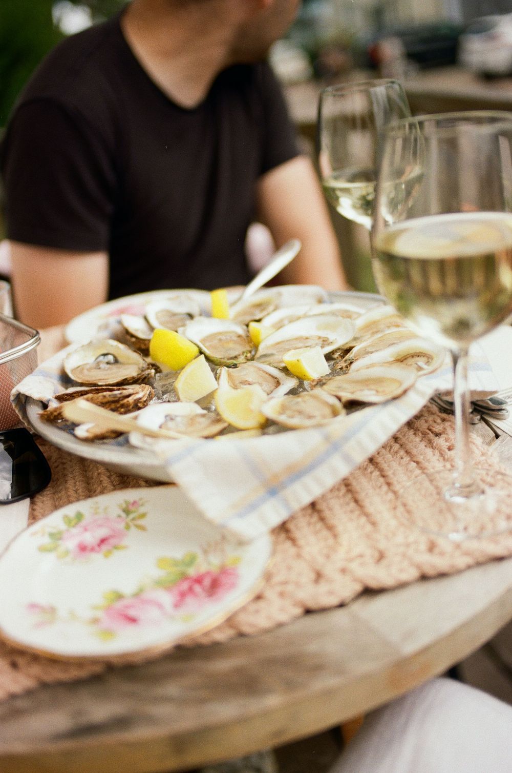 Fresh raw oysters served on ice with lemon wedges and condiments on elegant floral-patterned plates.