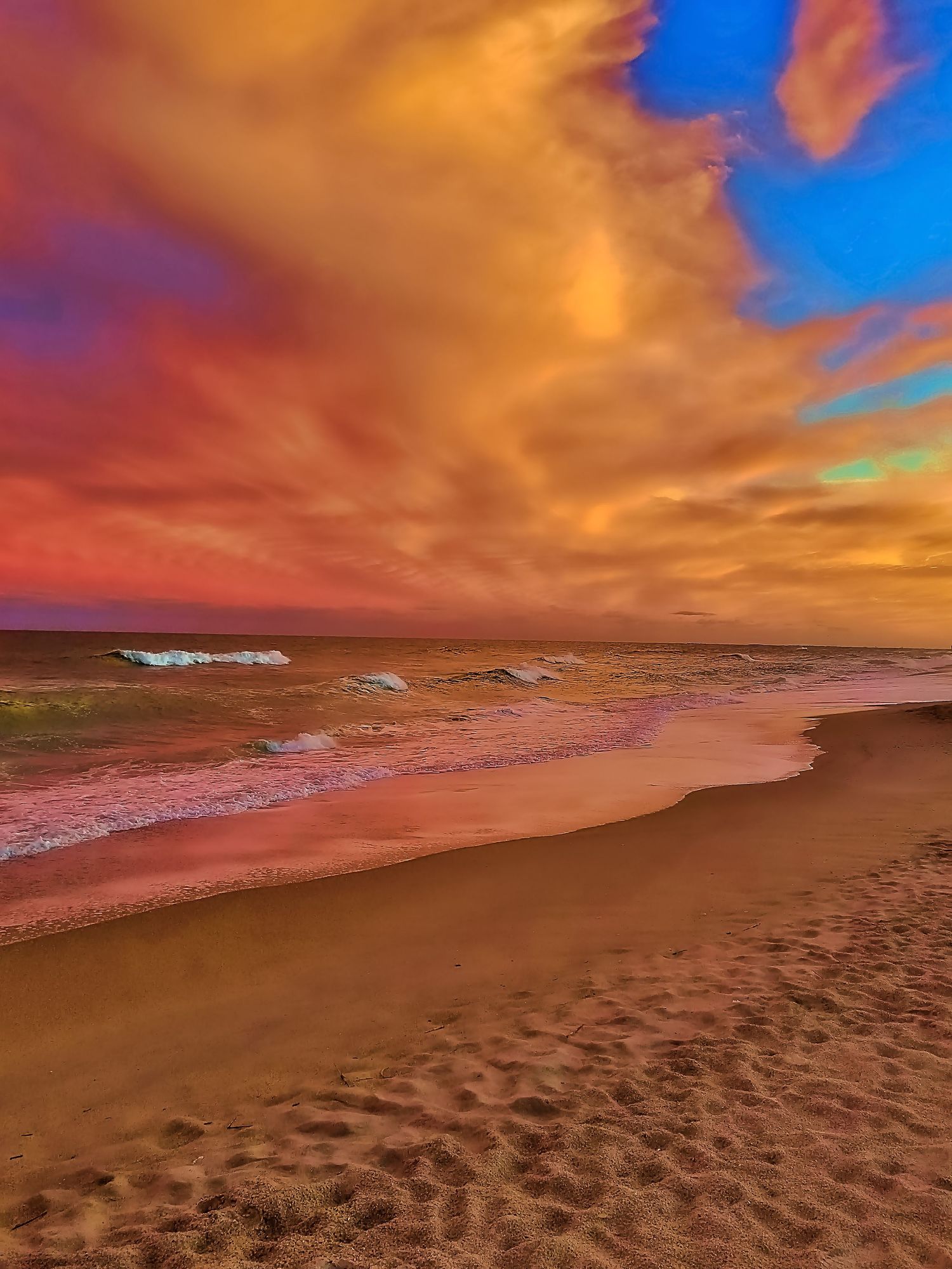 Dramatic orange sunset sky over sandy beach with crashing waves.