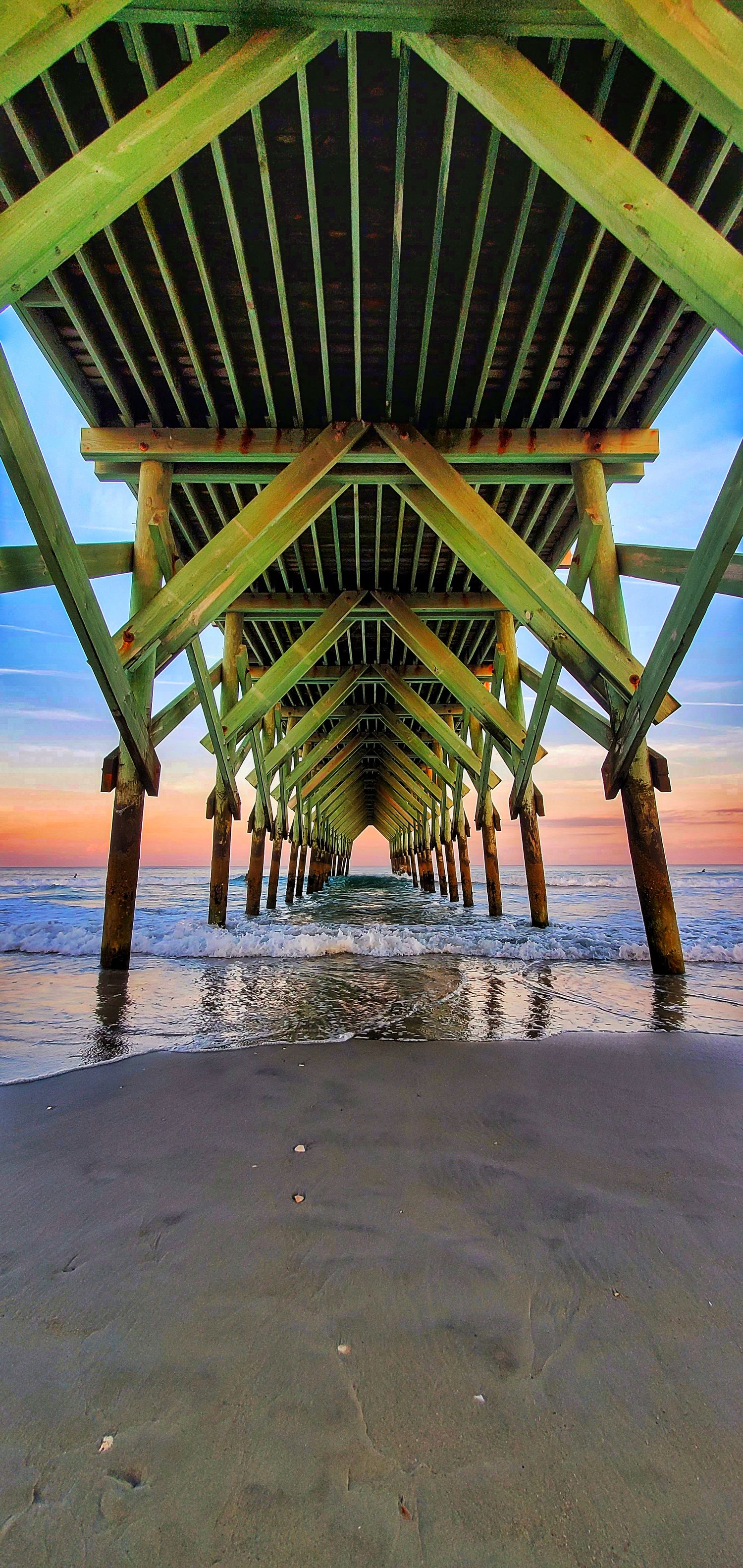 Wooden pier extends into ocean at sunset creating symmetrical tunnel effect.