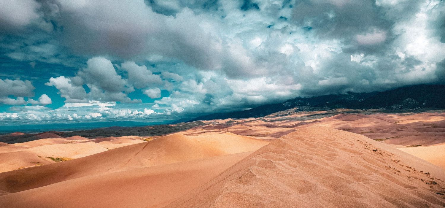 Stunning sand dunes under dramatic turquoise sky with storm clouds approaching.