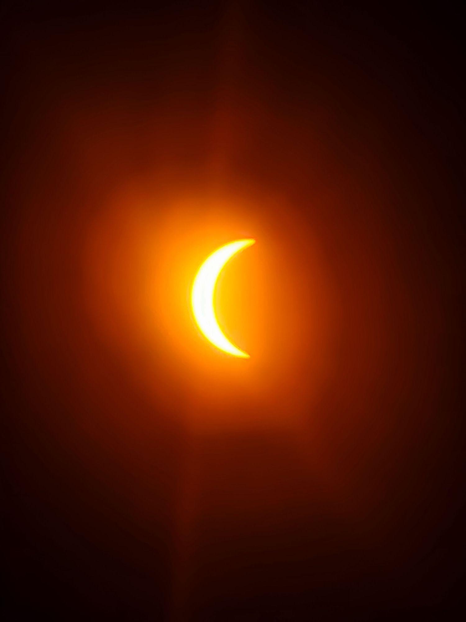 A partial solar eclipse shows a bright crescent sun against a dark orange sky.