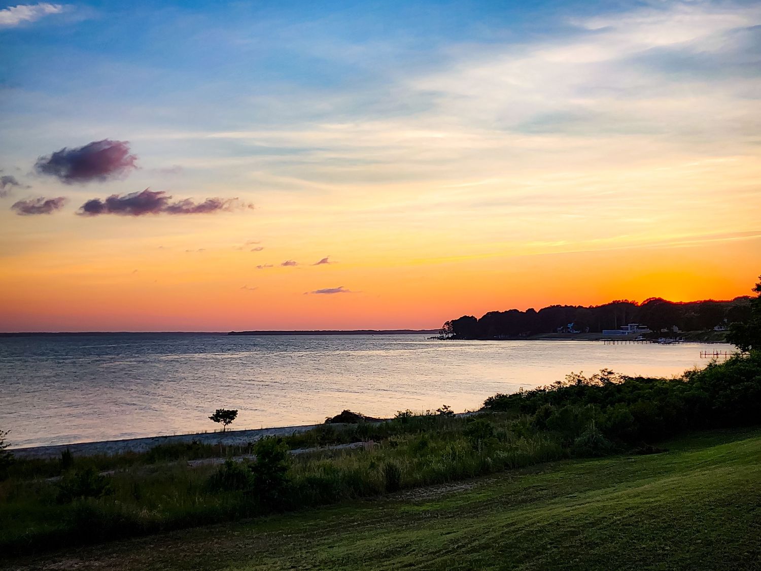 Stunning coastal sunset over the ocean with silhouetted shoreline and grassy foreground.