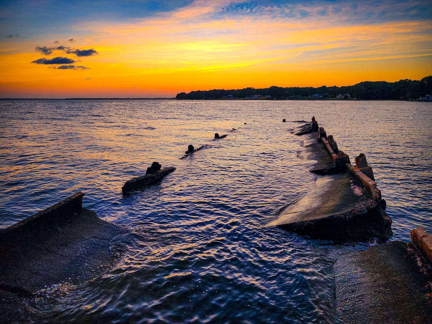 Old wooden pier posts silhouetted against a vibrant orange sunset over ocean waters.
