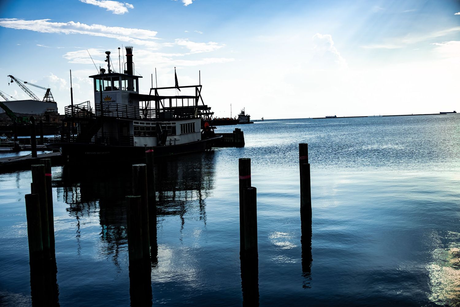 Scenic waterfront dock with silhouetted posts and industrial structures reflected in calm blue waters at dusk.