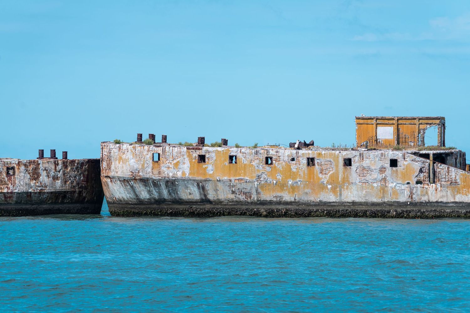 A panoramic view of an old stone fortress wall along turquoise blue waters under a bright sunny sky.