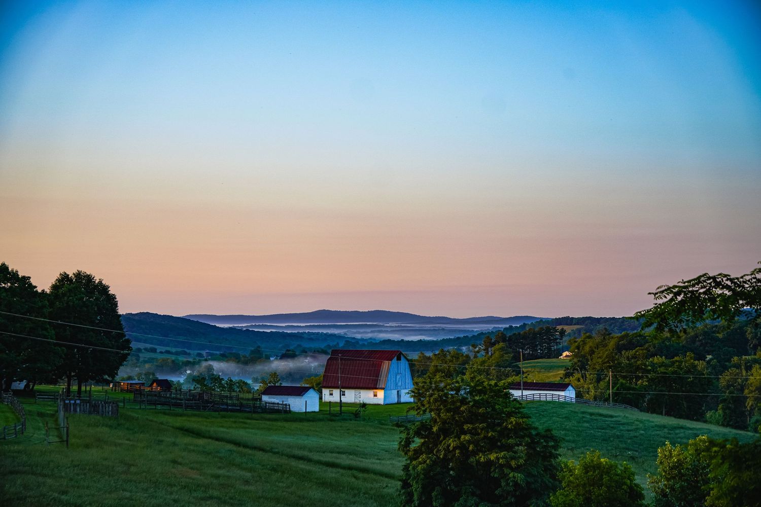 Peaceful countryside landscape with white buildings and barns set against blue twilight sky.