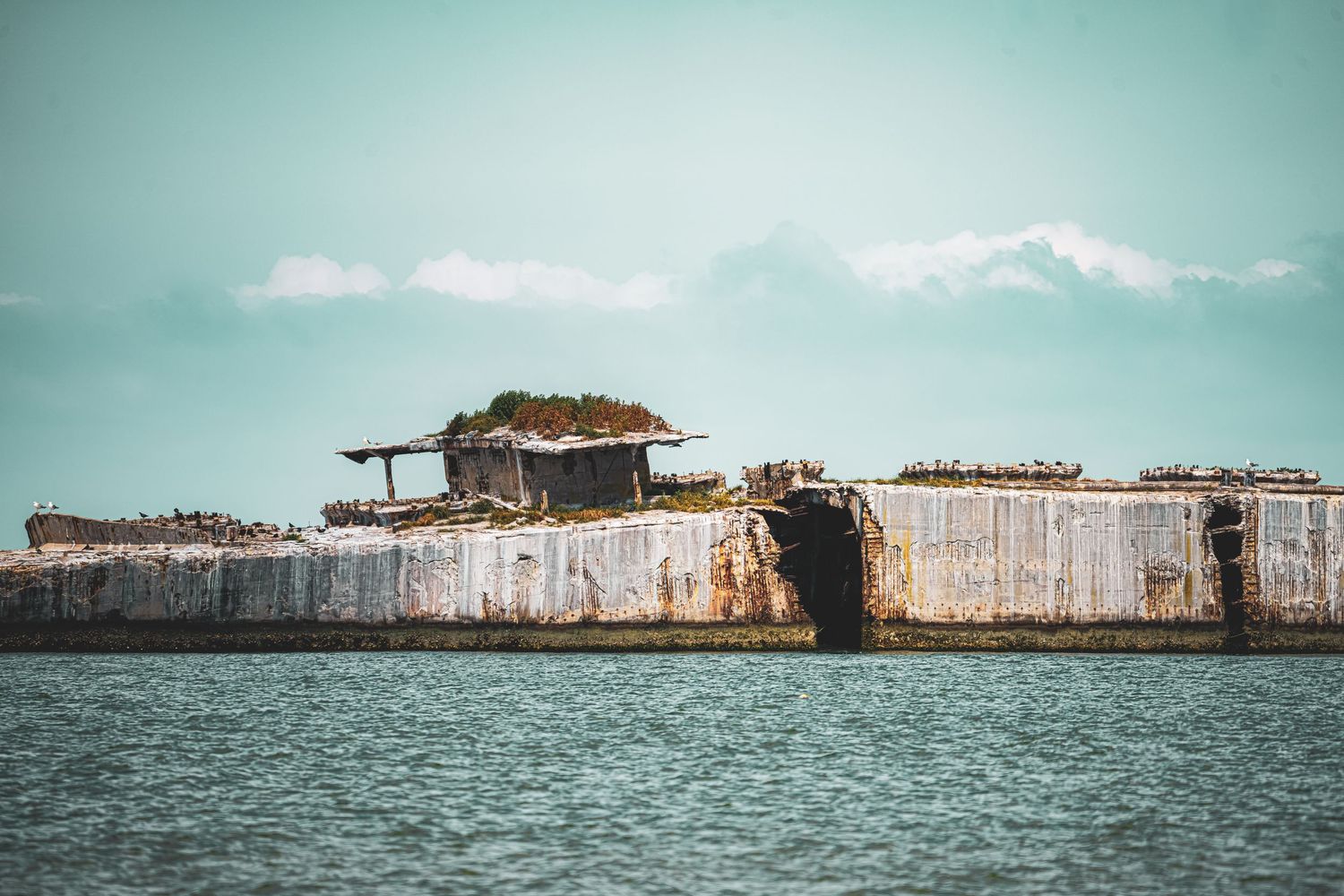 Scenic panoramic view of an old abandoned wooden fort structure in the ocean against a cloudy turquoise sky.