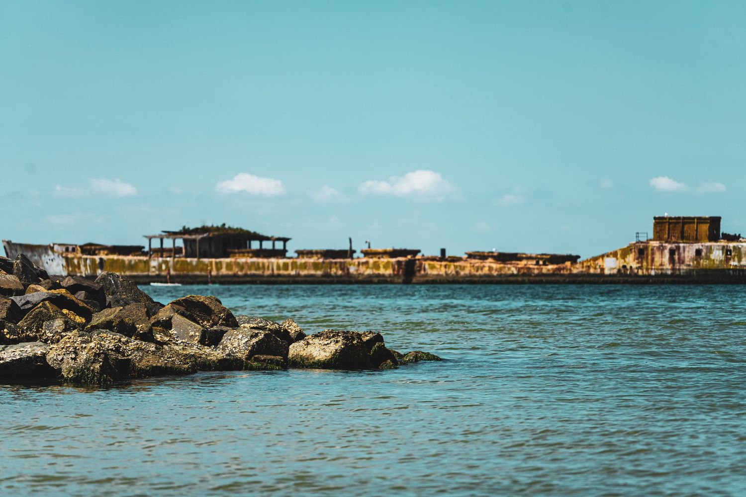 Wide angle seascape showing weathered buildings on a rocky coast with calm turquoise waters.