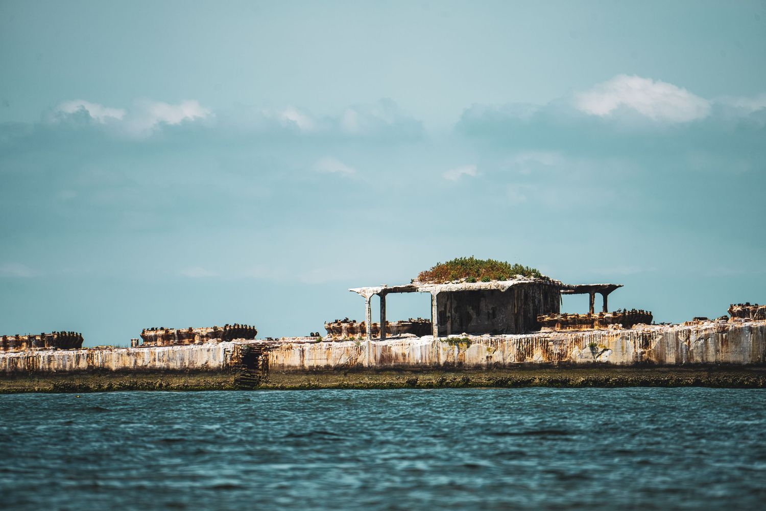 An abandoned concrete pier with a weathered structure sits against a turquoise sky and calm waters.