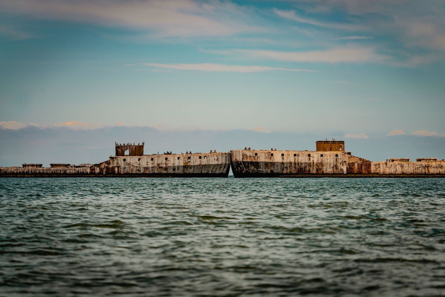 A panoramic view of a distant cityscape across rippling water under a cloudy sky with a blue tint.