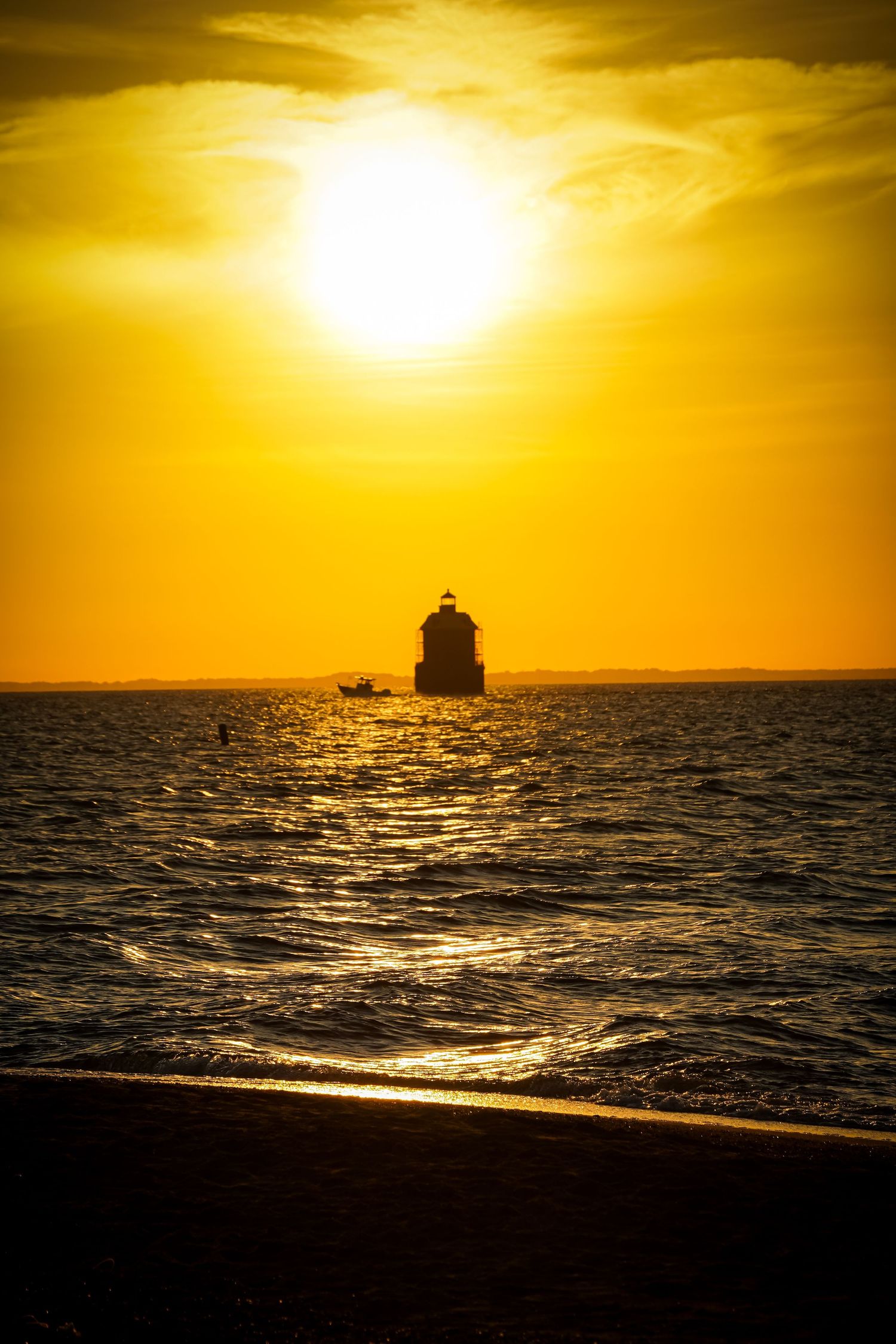 A silhouetted lighthouse stands against a brilliant golden sunset over rippling ocean waters.